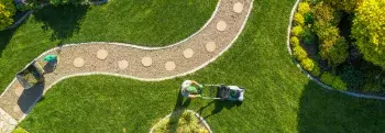 Foto van een tuin met een paadje door en een tuinman aan het werk